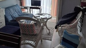 Un salon comprenant un canapé, un fauteuil en osier, une table en verre, un téléviseur et un lustre.