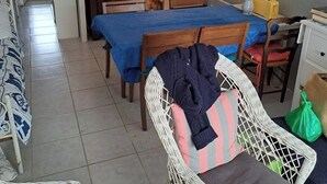Une pièce de taille modeste comprenant un lit, une table à manger, une chaise en osier et un coin cuisine.