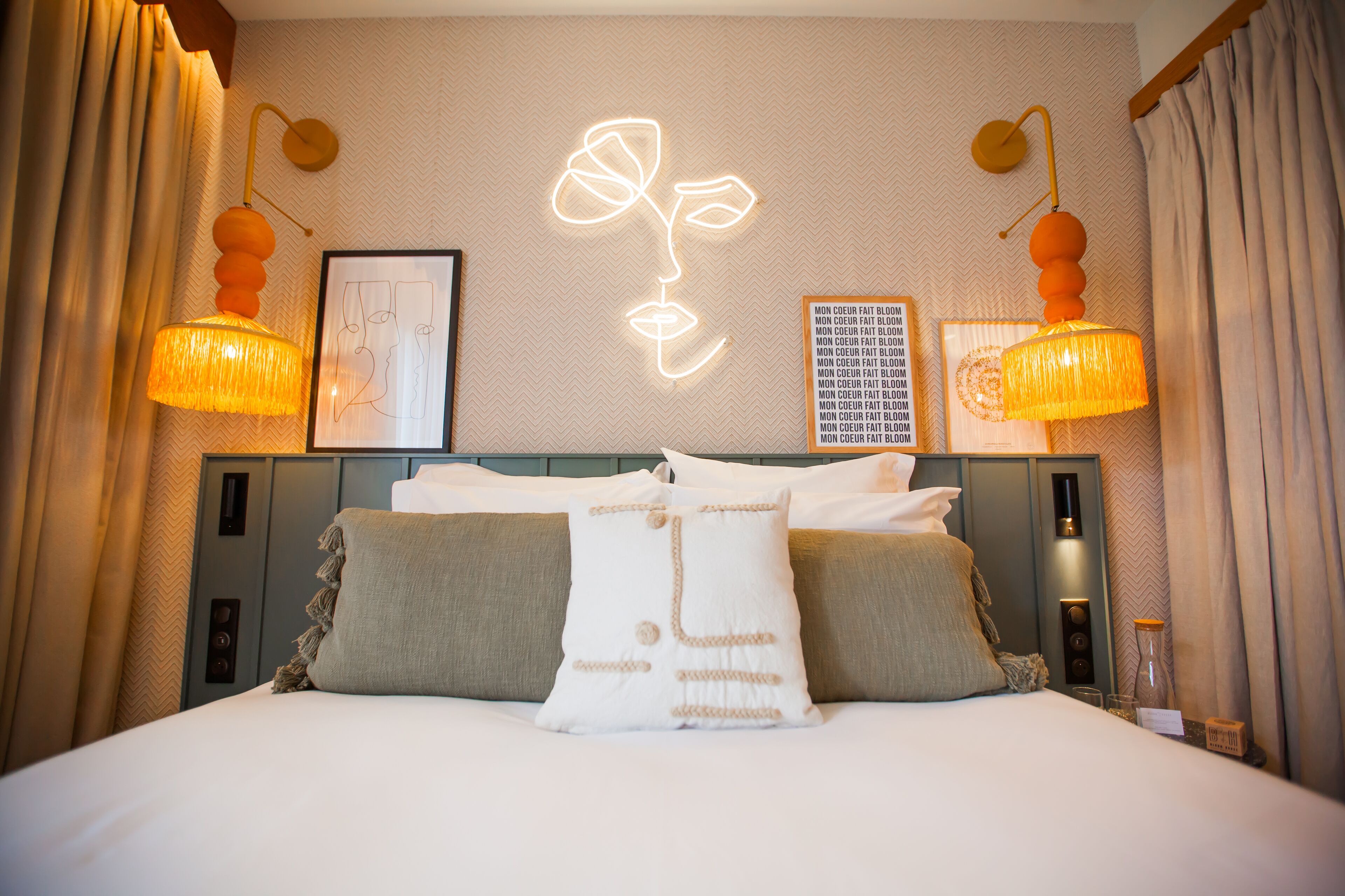 A neatly made bed with pillows, a wall art of a flower, and two wall-mounted lamps.