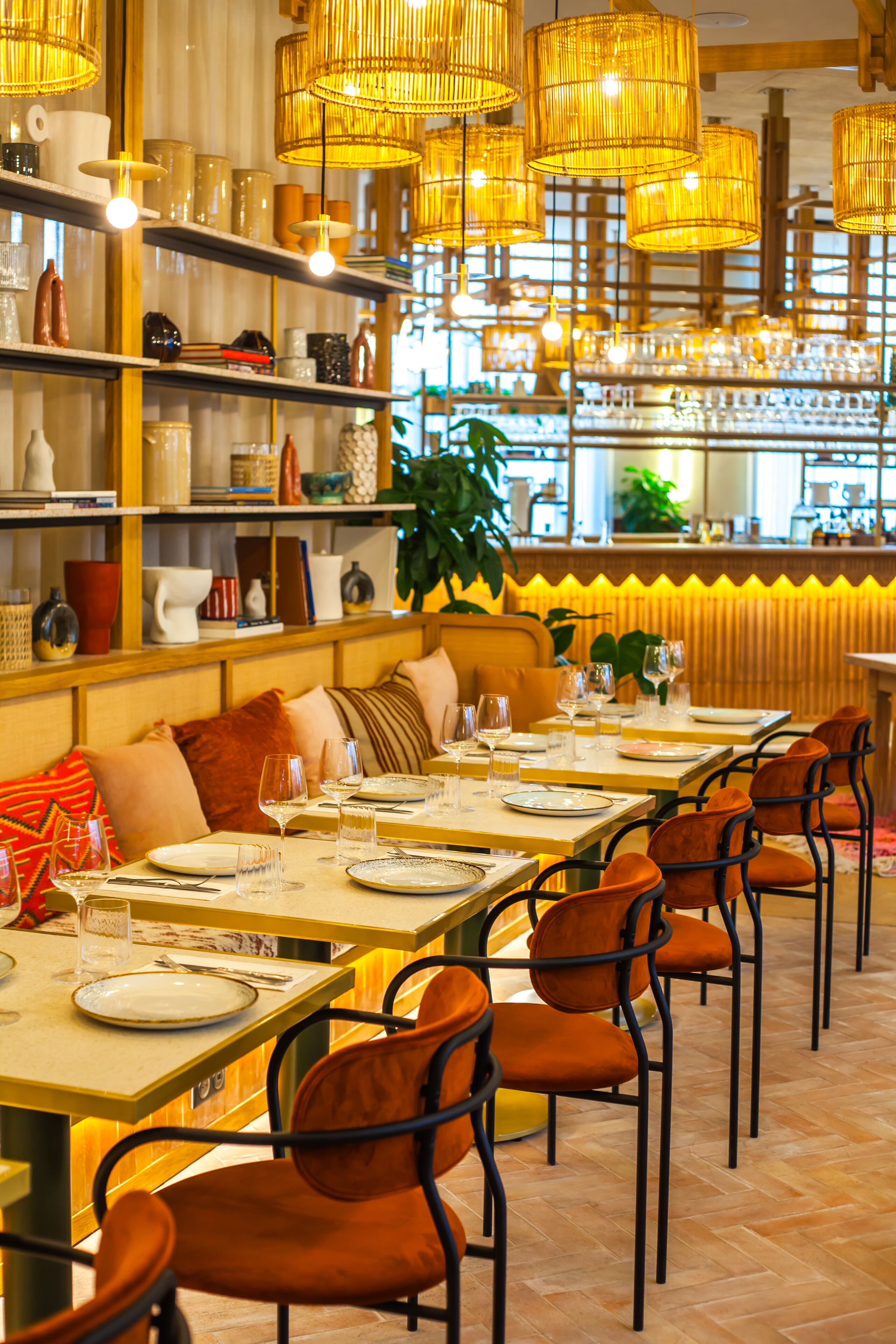 Un ristorante con diversi tavoli apparecchiati, scaffali con vari oggetti e lampade di vimini appese.