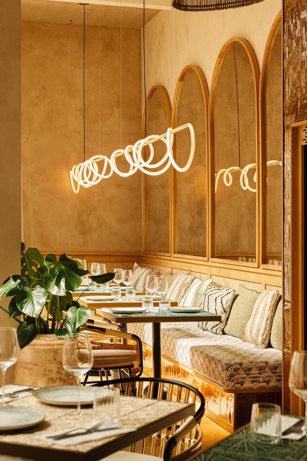 Un restaurante con ambiente cálido, que presenta una larga mesa compartida, asientos acolchados y una lámpara moderna.