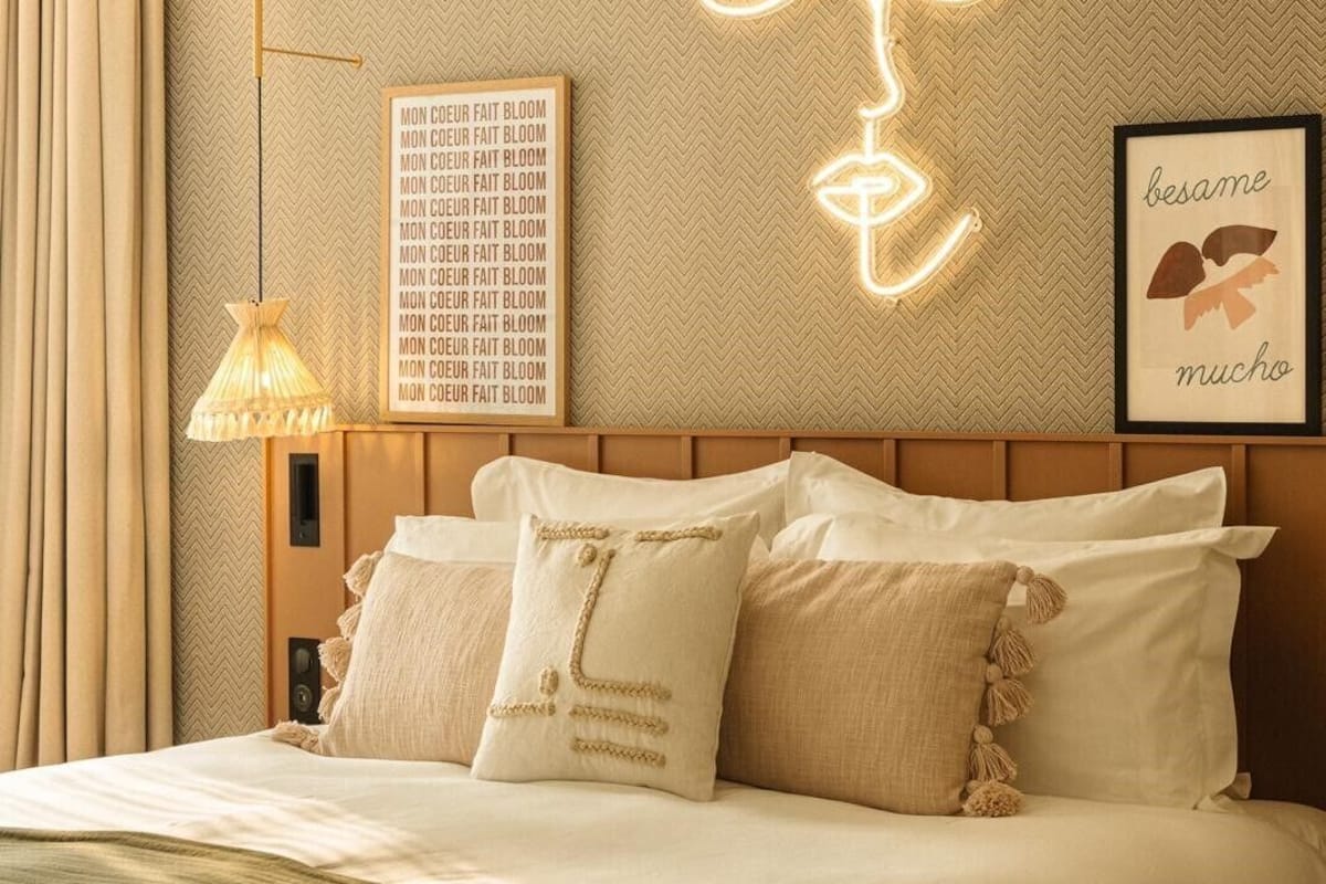 A hotel room with a bed, a wall-mounted light fixture, and a decorative wall piece.
