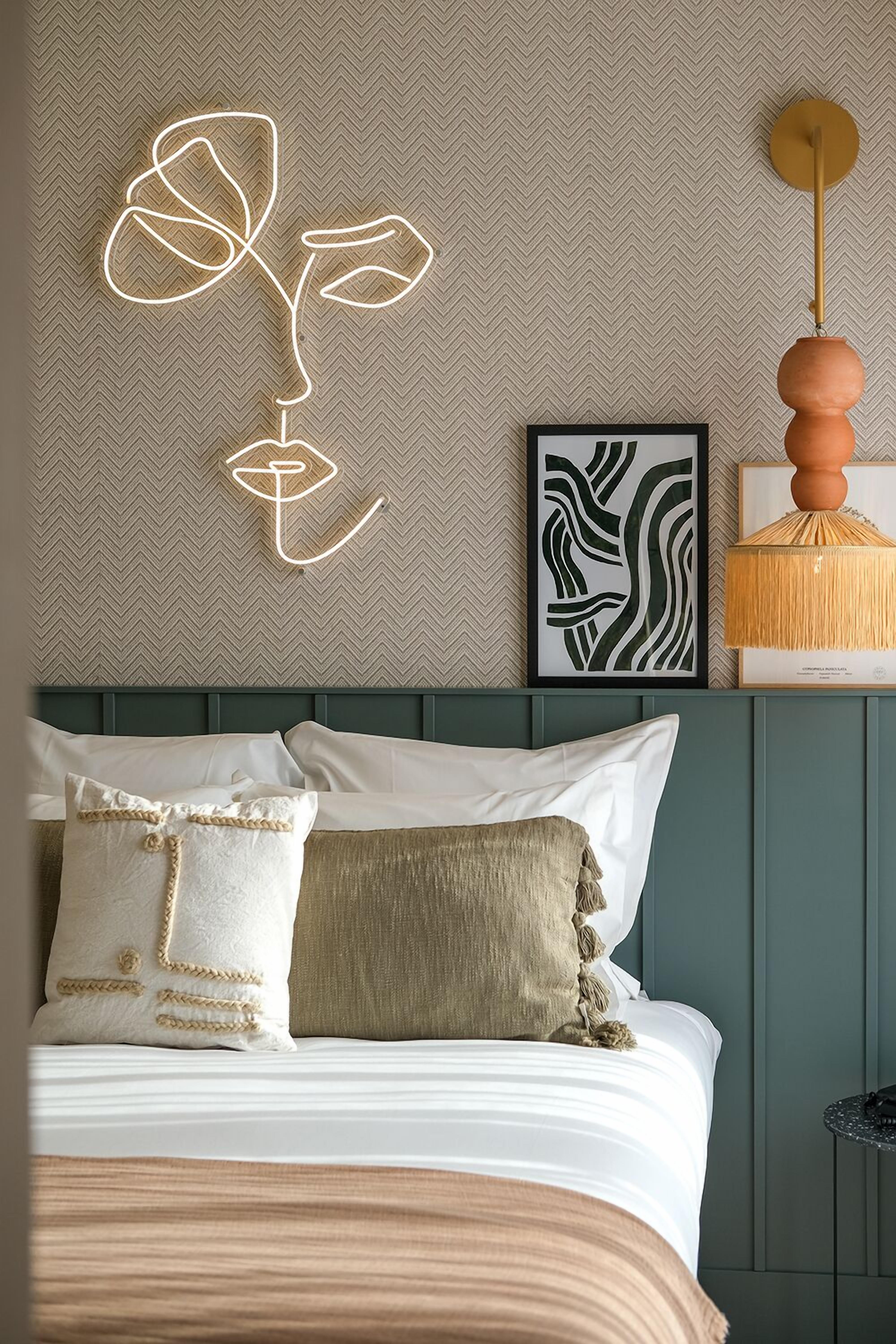 A neatly made bed with white and beige bedding, a decorative wall art piece, and a modern lamp.