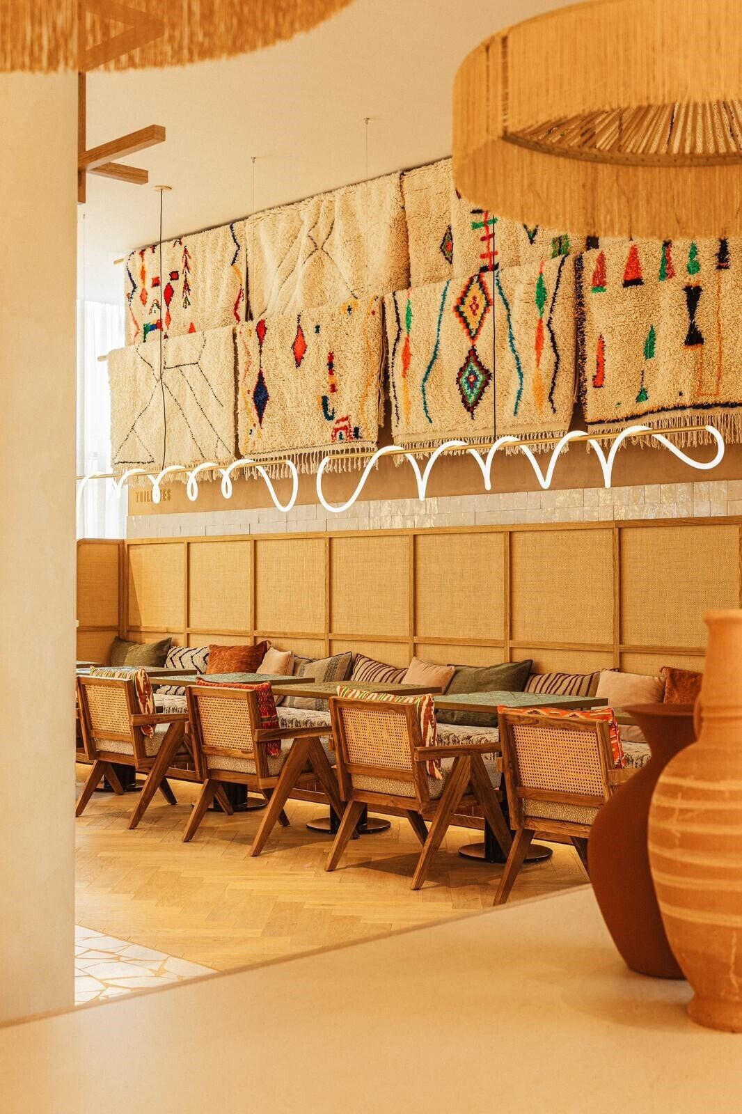 A room with a long sofa, wooden chairs, and a woven tapestry on the wall.