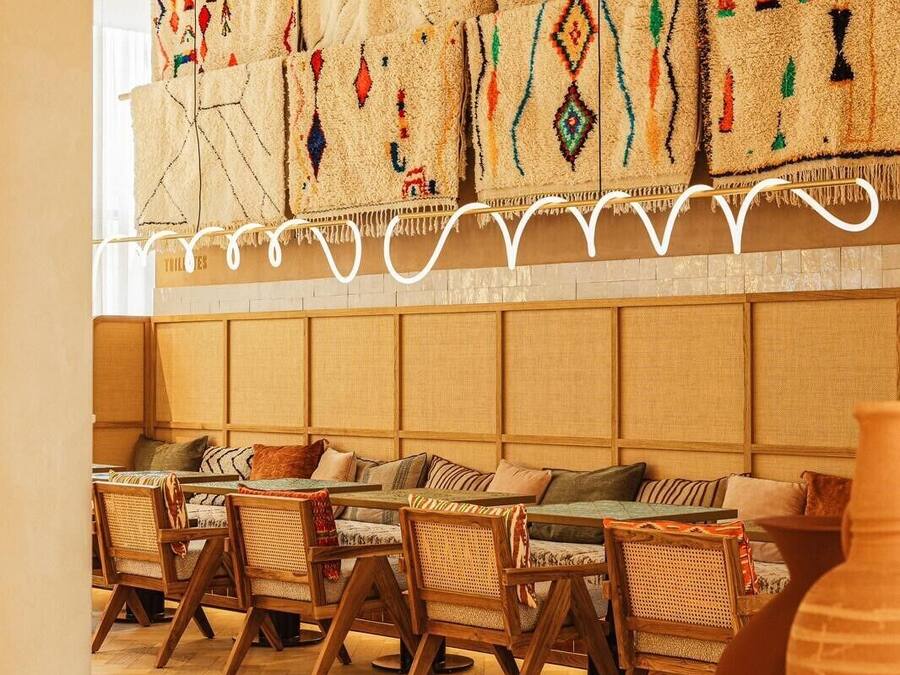 A room with a long sofa, wooden chairs, and a woven tapestry on the wall.