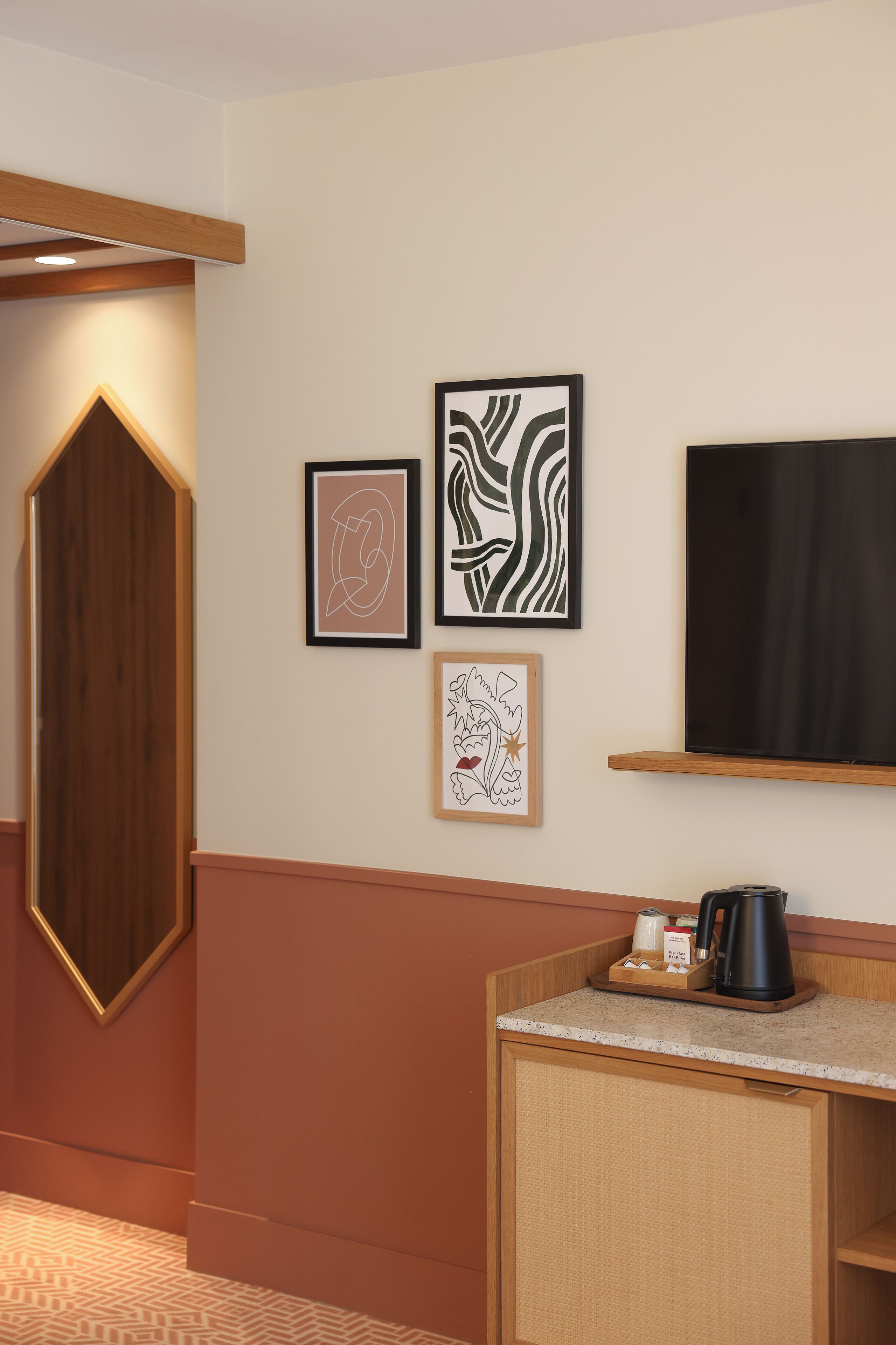 Une chambre d’hôtel avec un meuble en bois, une machine à café et des œuvres d’art encadrées accrochées au mur.