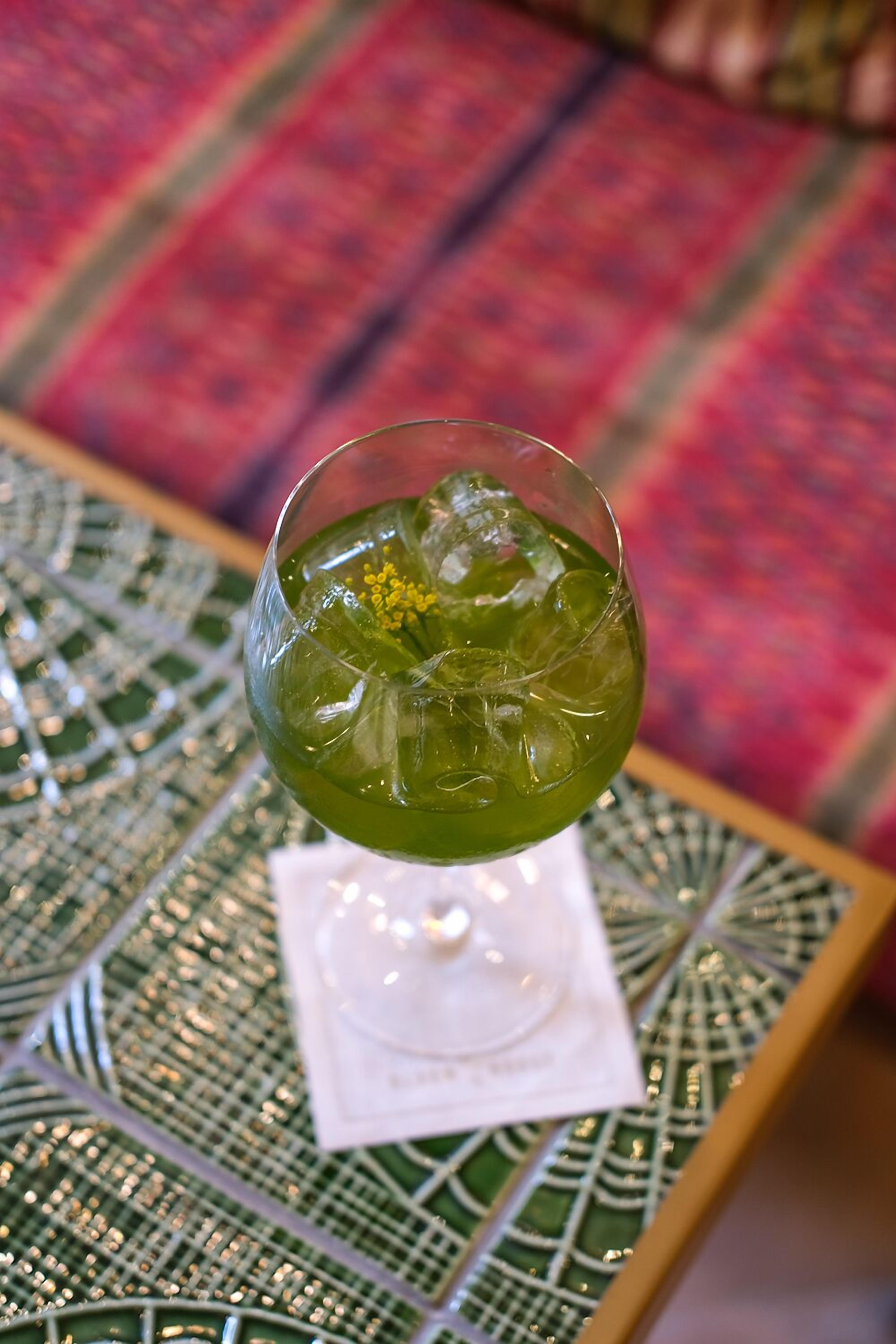 A cocktail glass with a green drink on a table with a decorative glass top.