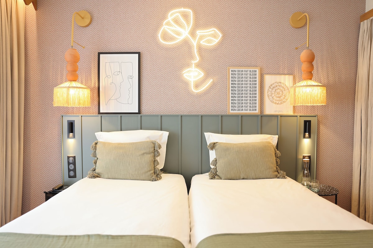 A hotel room with two beds, a neon flower wall art, and a framed picture.