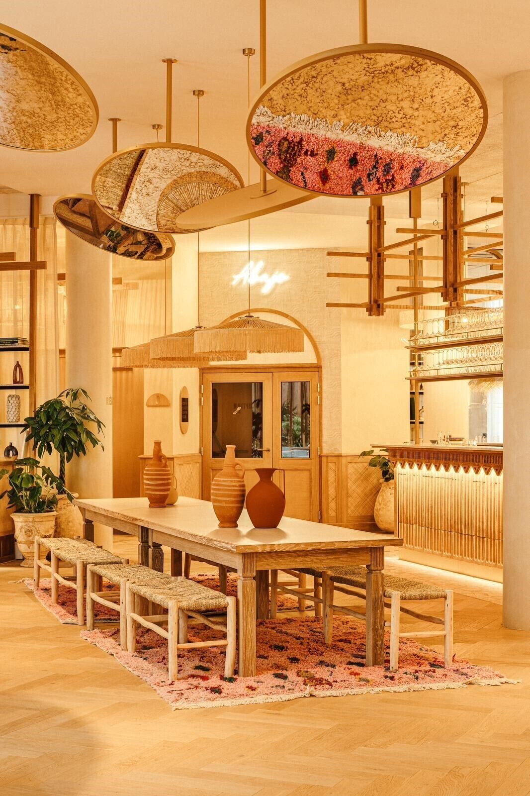 Un interno di ristorante con un tavolo di legno, panche, lampade a sospensione e una zona bar.