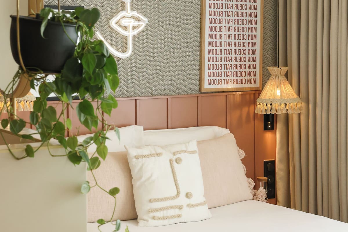 A neatly arranged bedroom with a bed, a wall-mounted plant, a decorative light, and a framed text on the wall.