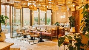 A cozy restaurant with wicker hanging lights, wooden furniture, and large windows offering a view of the outdoors. - Bloom House Hotel & SPA (Paris)