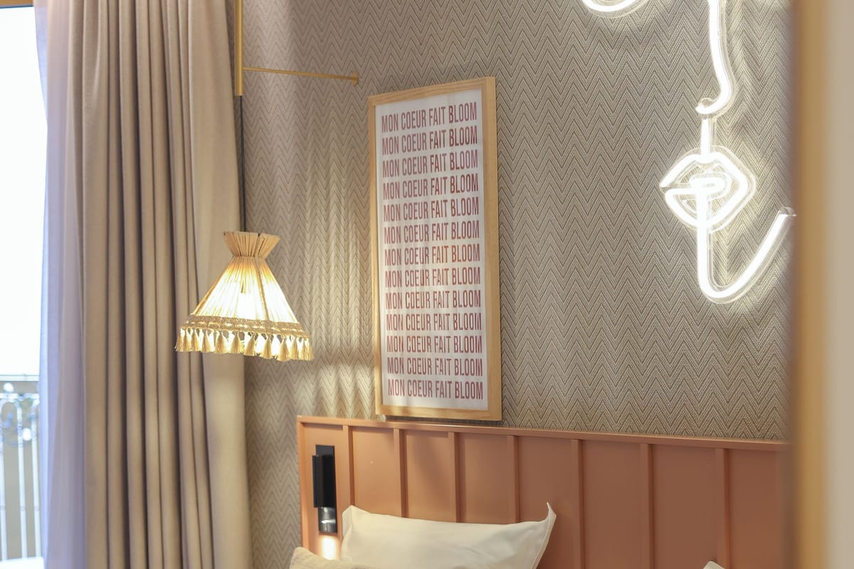 A neatly made bed with white linens and a headboard, a wall-mounted light fixture, and a framed text on the wall.