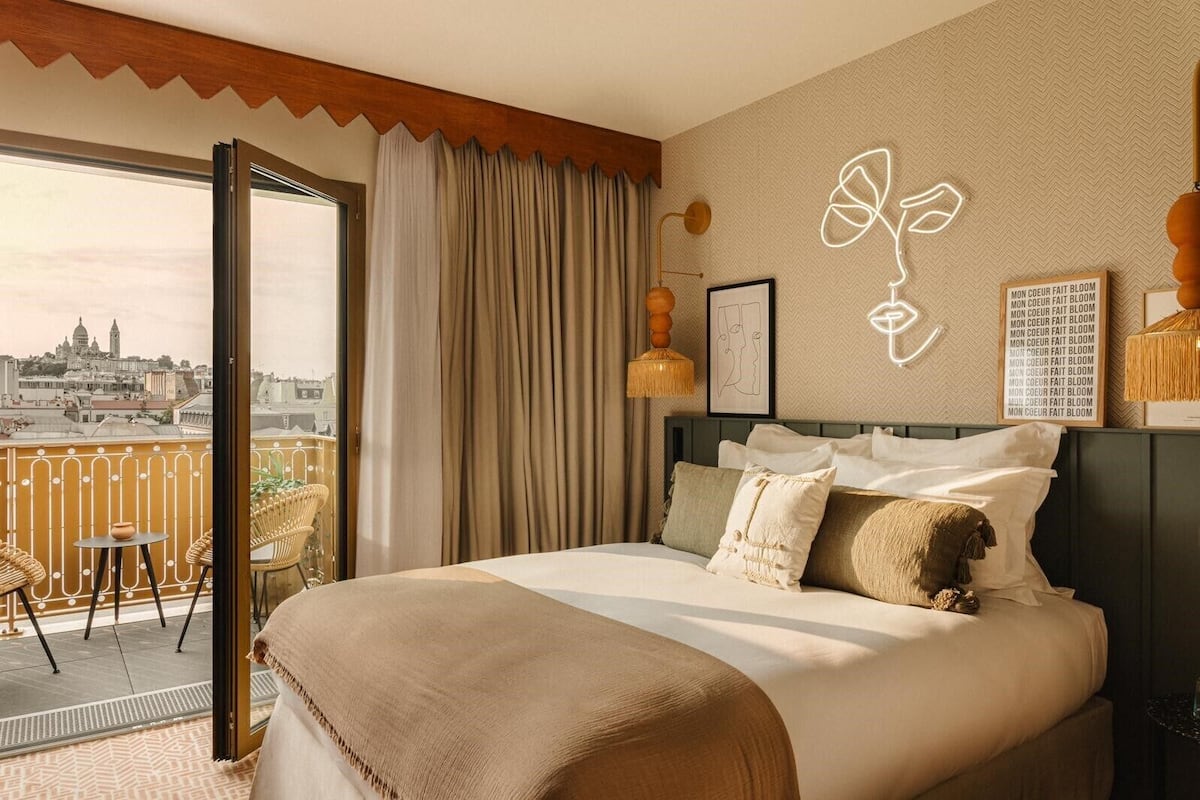 A hotel room with a bed, a view of the city, and a balcony with chairs and a table.