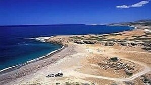 Vista aérea de un paisaje costero con cielo despejado, un camino sinuoso y una masa de agua.