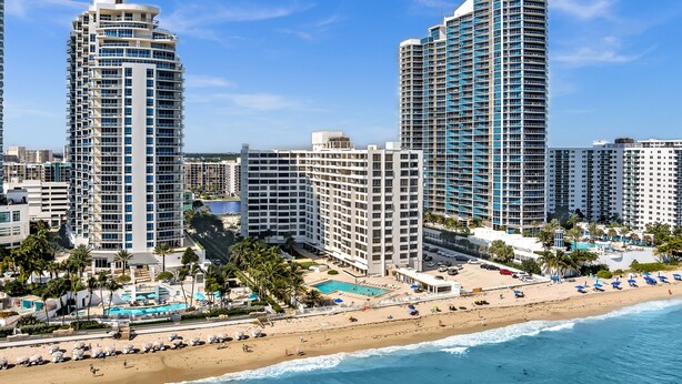 A beachfront hotel with multiple high-rise buildings, a pool area, and a beach with umbrellas.
