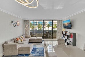 A modern living room with a sectional sofa, a coffee table, and a TV mounted on the wall. - Stylish Beachfront Gem ~ Sea View, Pool, Gym, Pkg! (Hollywood)