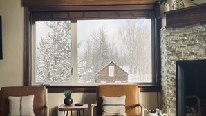 A cozy room with two leather armchairs, a small table with a plant, and a large window overlooking a snowy landscape. - Newly Updated, Cozy and Spacious Condo! (Frisco)