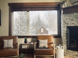 A cozy room with two leather armchairs, a small table with a plant, and a large window overlooking a snowy landscape. - Newly Updated, Cozy and Spacious Condo! (Frisco)