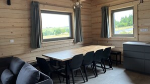 En trästuga med en matplats, stolar, en soffa och två fönster med gardiner.