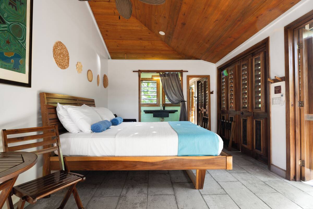A wooden-framed bed with white and blue bedding, a wooden chair, and a small table.