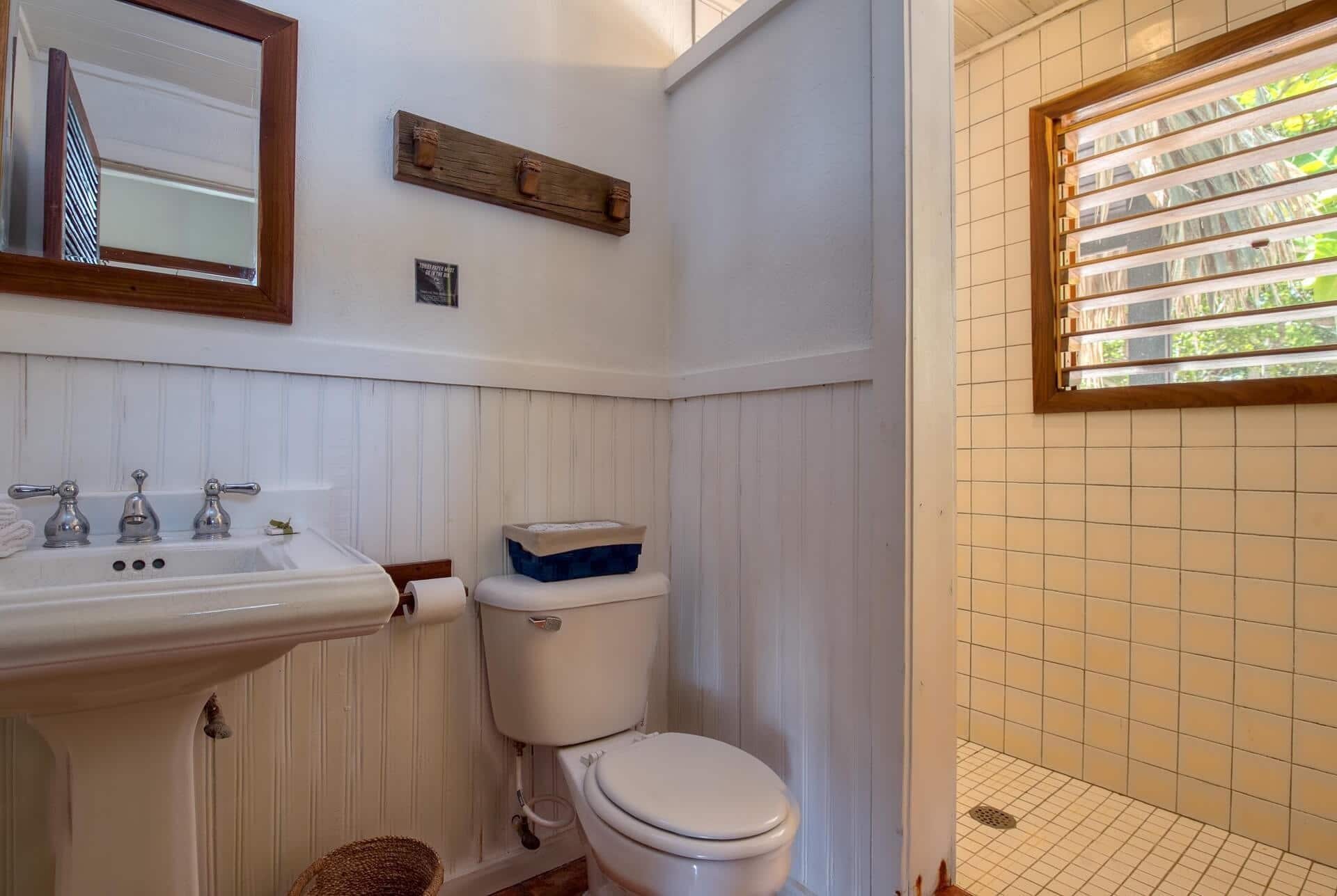 Een badkamer met een wit wastafel, drie kraanwerk, een toilet en een raam met jaloezieën.