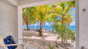 A beach view with palm trees, a chair with a backpack, and a clear blue ocean. - CAMP BAY LODGE (Roatan)
