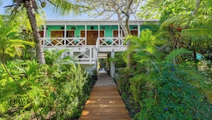 A wooden pathway leading to a building with a green facade and white railings. - CAMP BAY LODGE (Roatan)