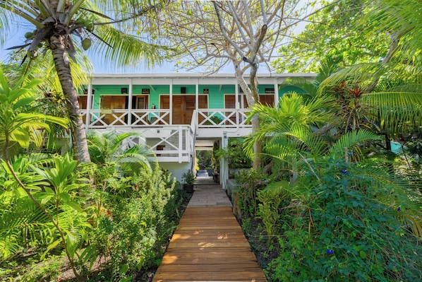 A wooden pathway leading to a building with a green facade and white railings. - CAMP BAY LODGE (Roatan)