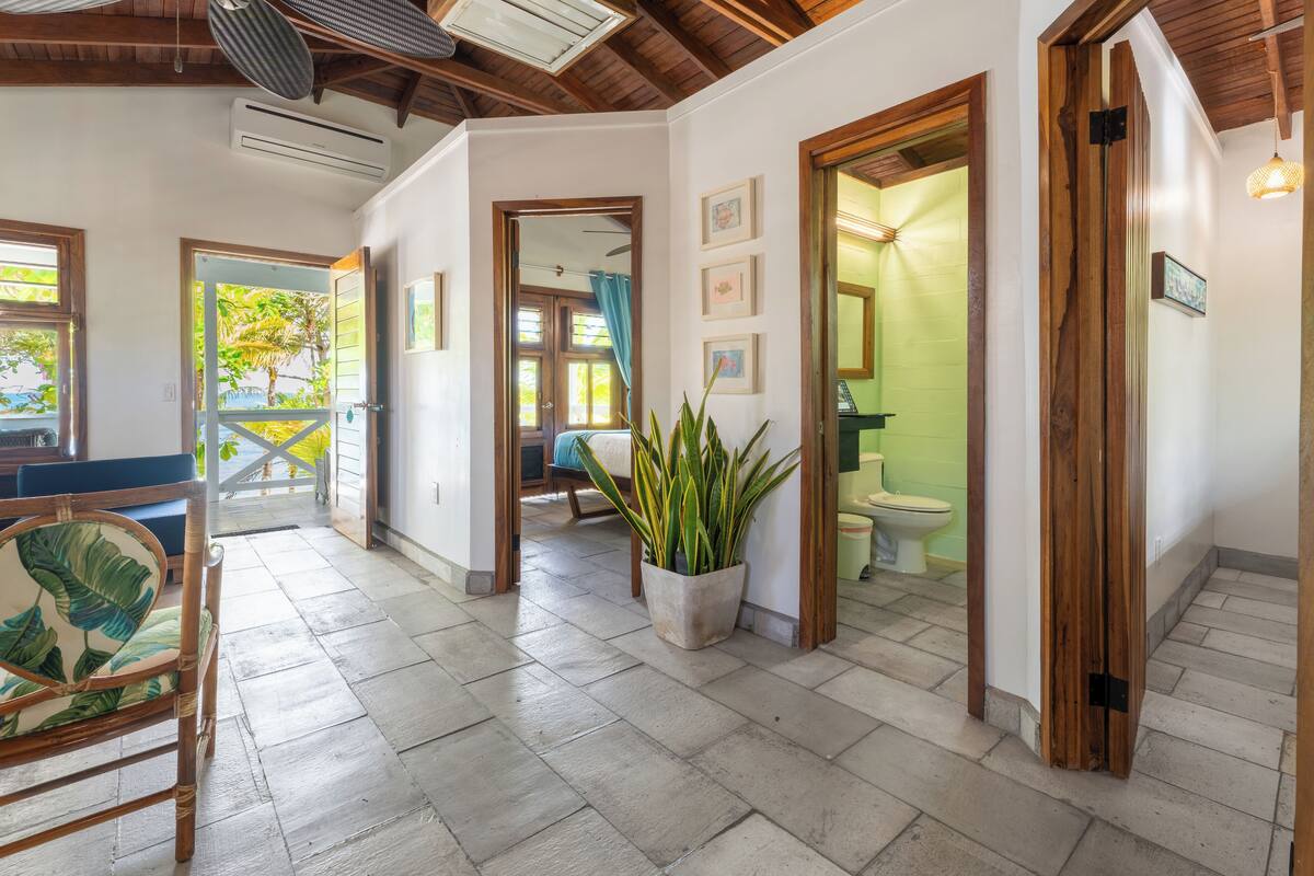 A spacious hallway with a wooden ceiling, a potted plant, and a view of a bathroom with a toilet and sink.