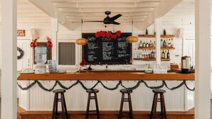 A bar area with a wooden counter, three stools, a blackboard menu, and a ceiling fan. - CAMP BAY LODGE (Roatan)