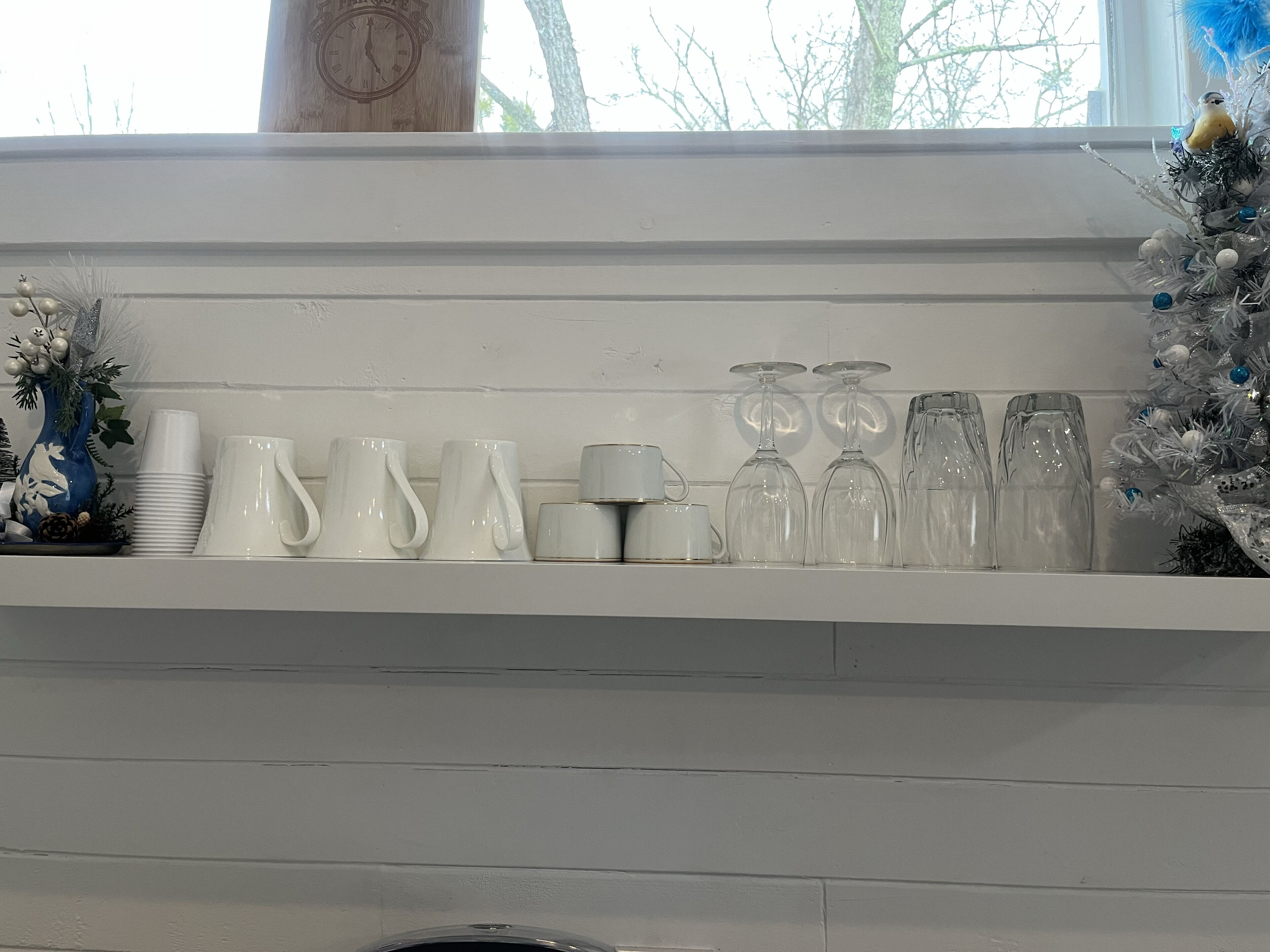 Een witte schoorsteenmantel met diverse witte glazen en een kleine blauwe vaas.
