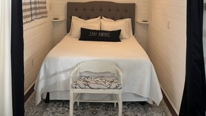 Une chambre à coucher avec un lit, un luminaire suspendu, une petite chaise et un tapis à motifs.