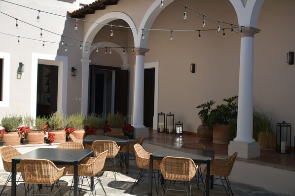 Une terrasse extérieure avec des tables et des chaises, des guirlandes lumineuses, des plantes en pot et un sol carrelé.