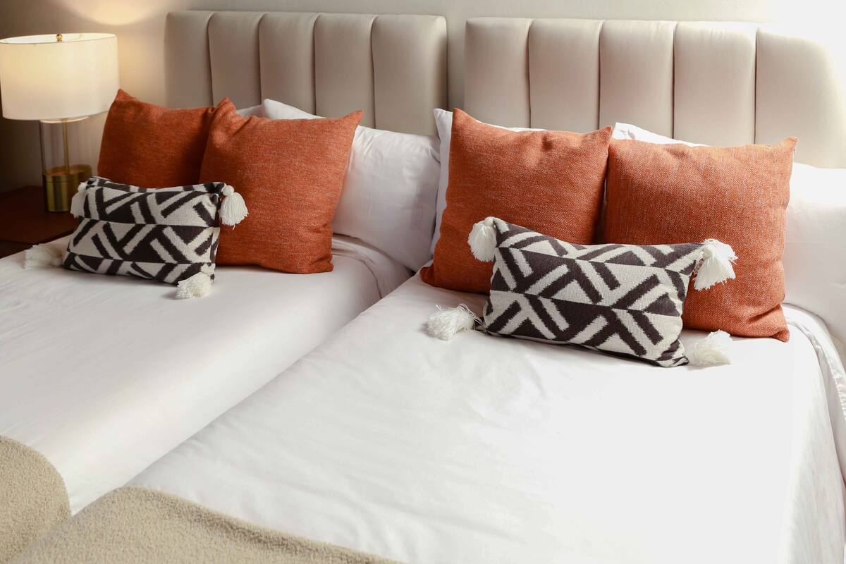 A bed with white linens and two pillows, one with a black and white pattern and the other with a solid color.
