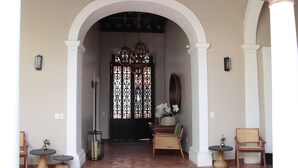 Una entrada con una puerta negra, columnas blancas y dos mesas redondas con sillas.