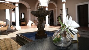 Una fuente en un patio con una mesa y sillas, un florero con una flor, y un edificio con arcos.