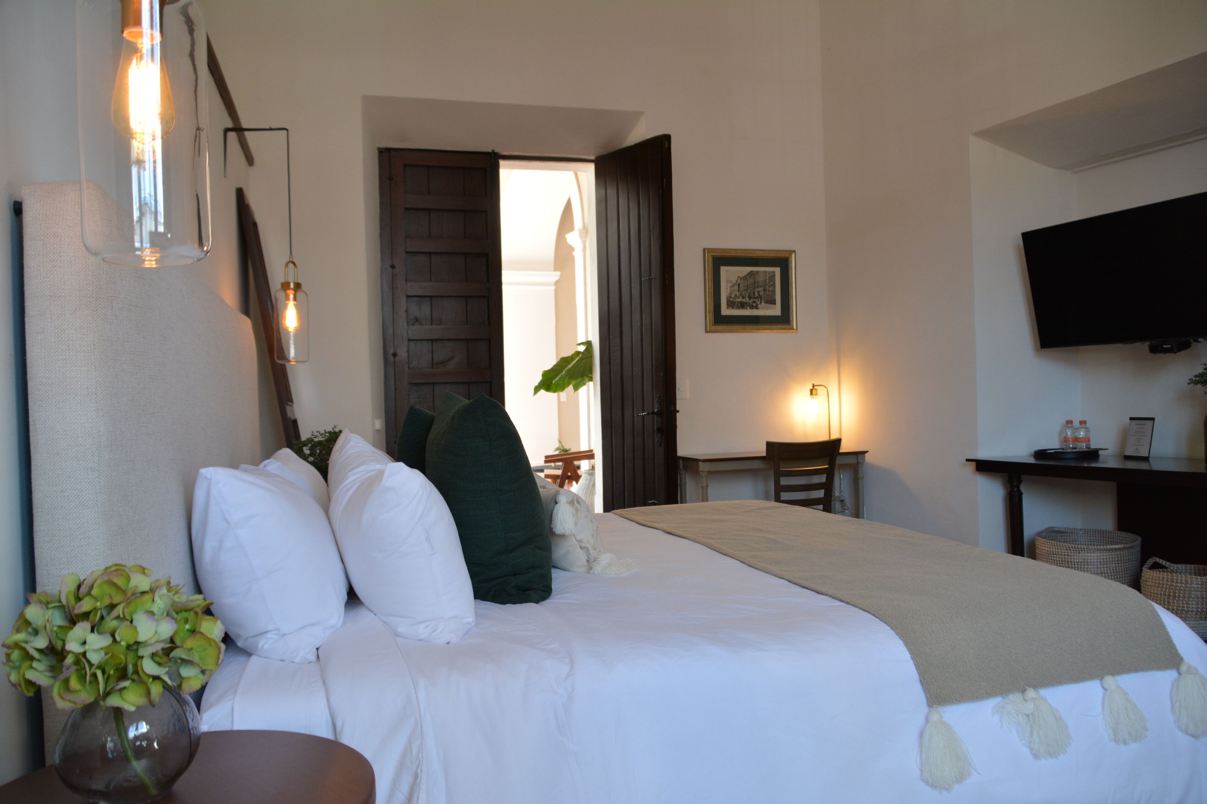 Habitación de hotel con una cama grande, un escritorio, un televisor y un florero con flores.
