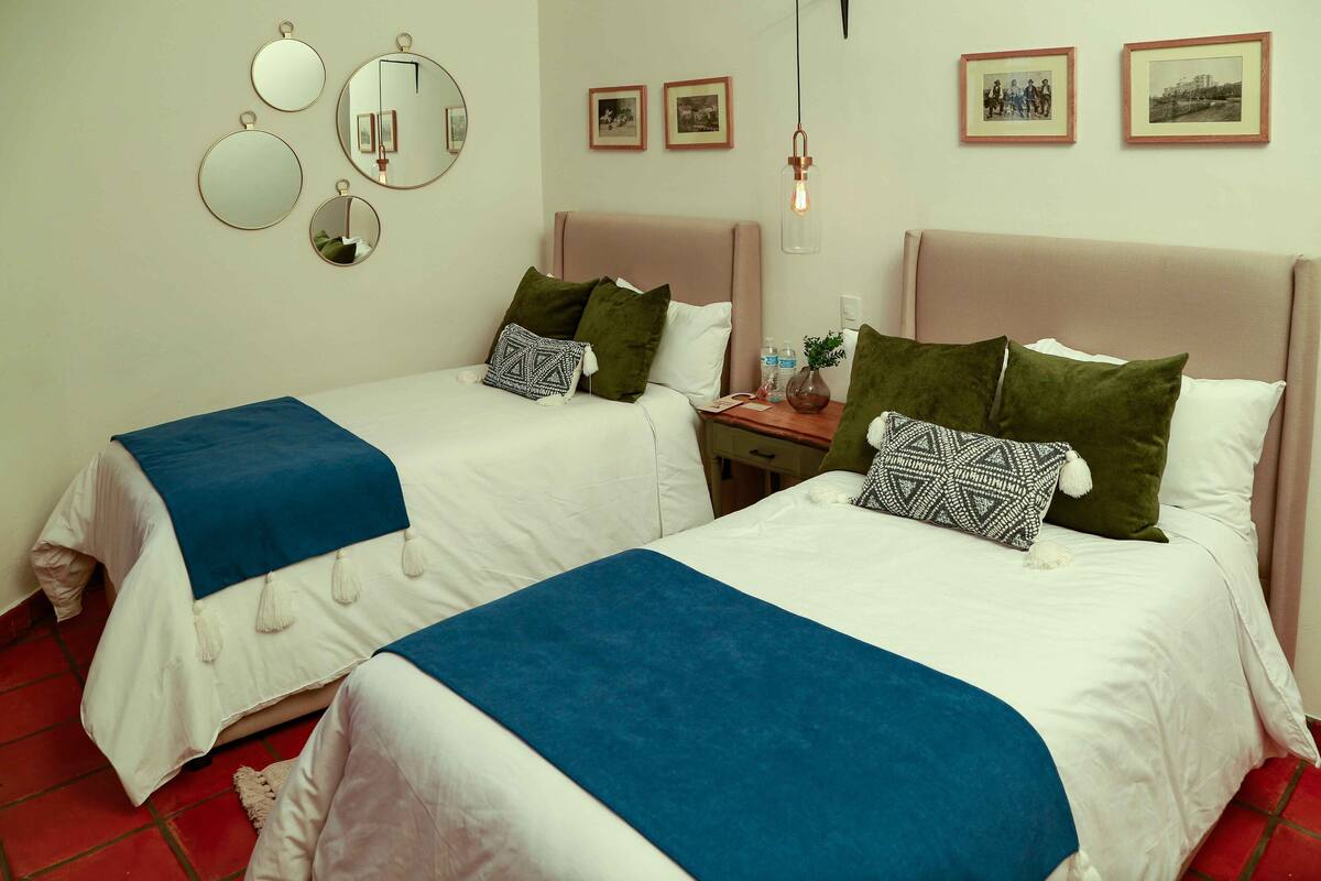 A hotel room with two beds, a nightstand, and a mirror.