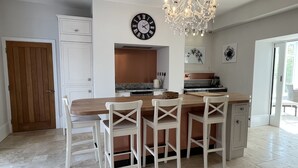A kitchen with a wooden island, white bar stools, a chandelier, and a clock on the wall. - Stunning and Luxurious Manor House Holiday Home (Dorchester)