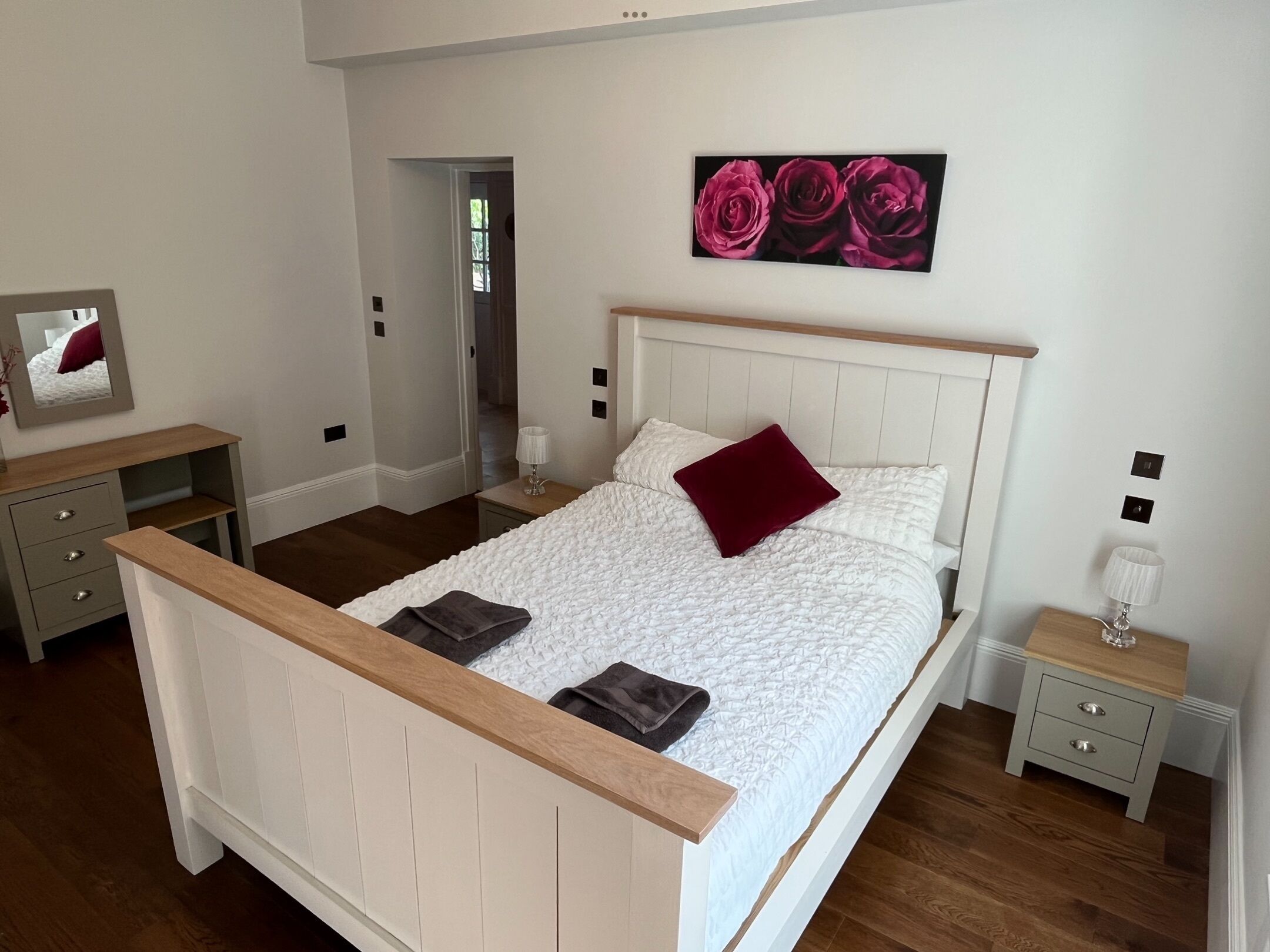 A bedroom with a bed, bedside tables, a dresser, and a painting of roses.