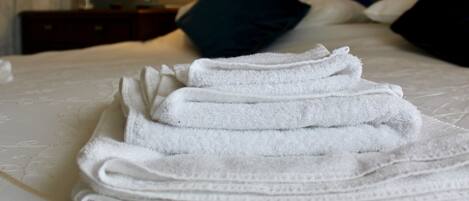Una cama bien hecha con toallas blancas dobladas, una lámpara de noche y una pared con un cuadro.