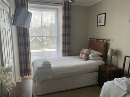 Una cama bien hecha con una almohada, una mesita de noche con una lámpara y una ventana con cortinas.