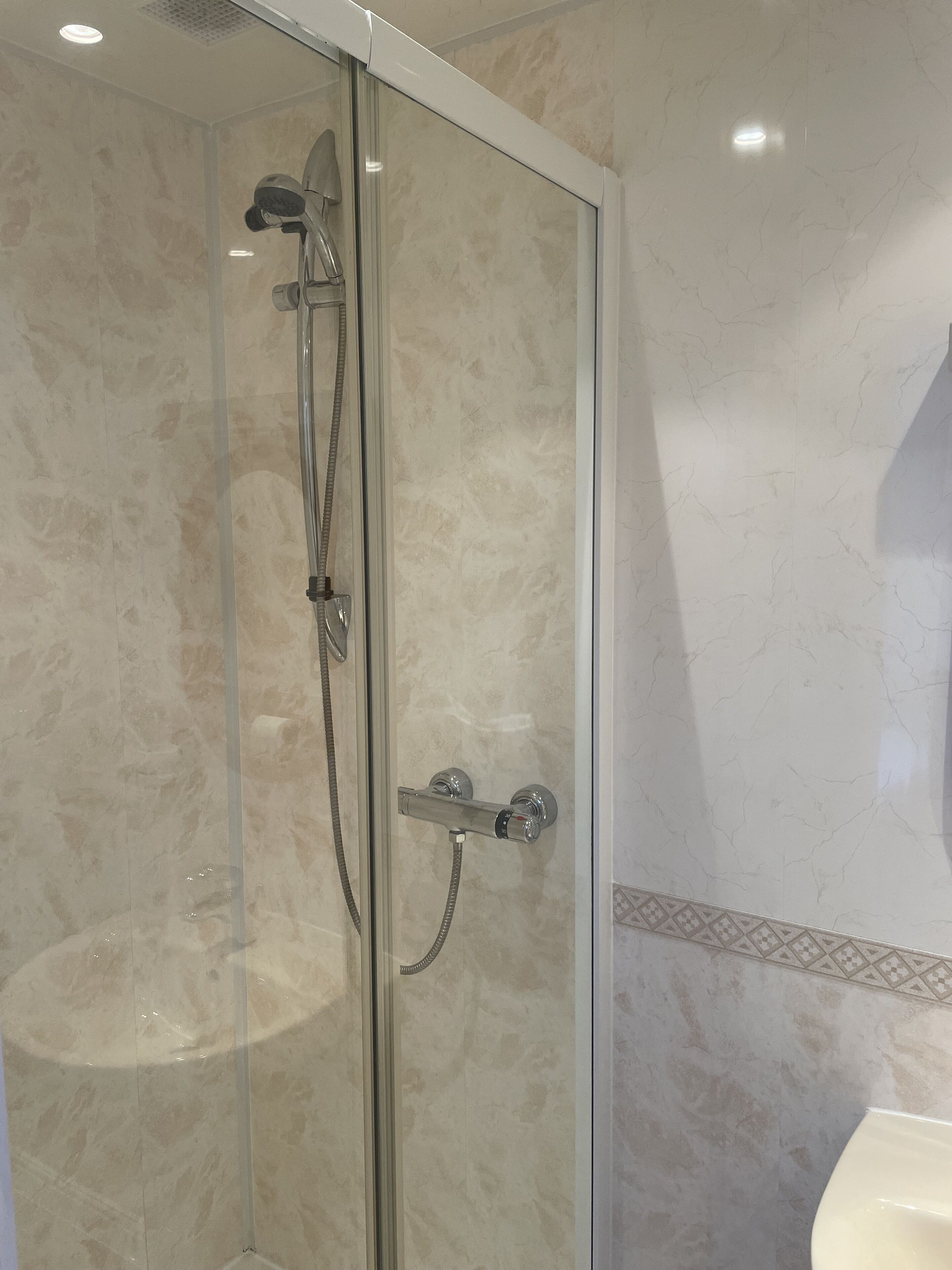 A glass-enclosed shower with a handheld showerhead and a wall-mounted faucet.
