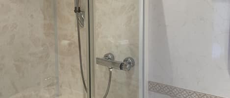 A glass-enclosed shower with a handheld showerhead and a wall-mounted faucet.