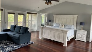 A bedroom with a large bed, a dark blue sofa, a patterned rug, and a ceiling fan. - The Chalet on Lake Wylie, 5000 sq ft, Sleeps16, Pet Friendly, Close to Charlotte (Belmont)