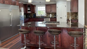 A modern kitchen with a central island, stainless steel appliances, dark wooden cabinets, and three bar stools. - The Chalet on Lake Wylie, 5000 sq ft, Sleeps16, Pet Friendly, Close to Charlotte (Belmont)