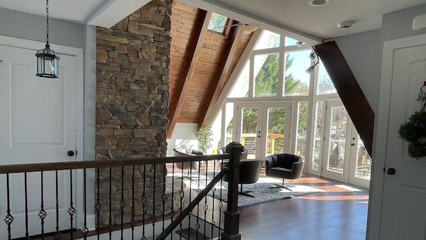A spacious room with a stone accent wall, a wooden staircase, and a view through large windows. - The Chalet on Lake Wylie, 5000 sq ft, Sleeps16, Pet Friendly, Close to Charlotte (Belmont)