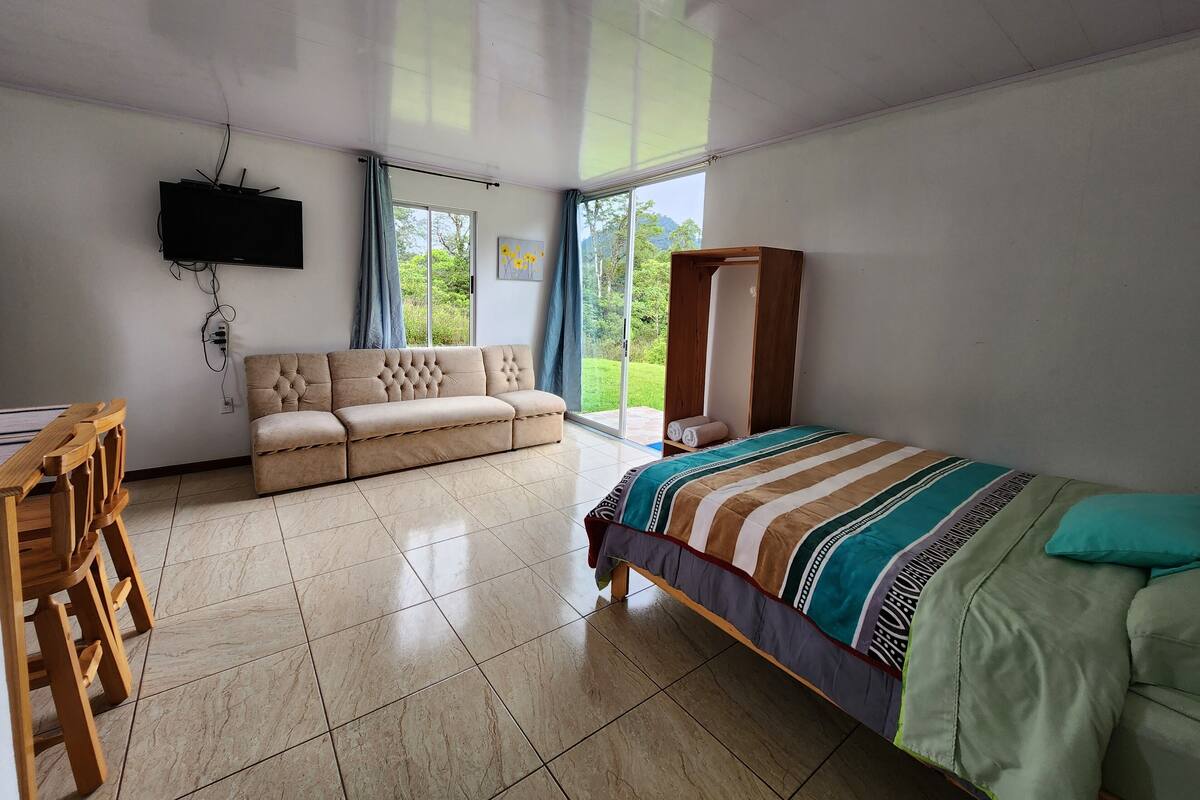 A bedroom with a bed, a sofa, a wooden desk, and a TV.