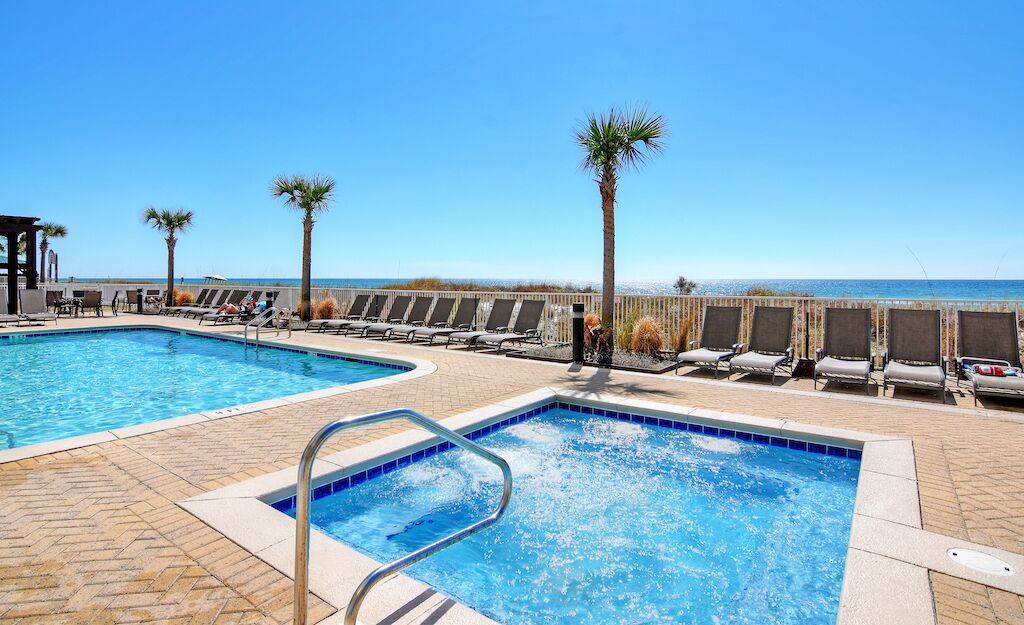 Zona de piscina con dos piscinas, sillas de descanso, palmeras y vista al océano.
