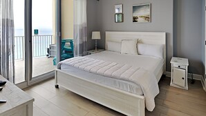 A bedroom with a large bed, a nightstand, a bedside table, and a view of the balcony. - Ocean Villa #2106 by Resort Collection (Panama City Beach)